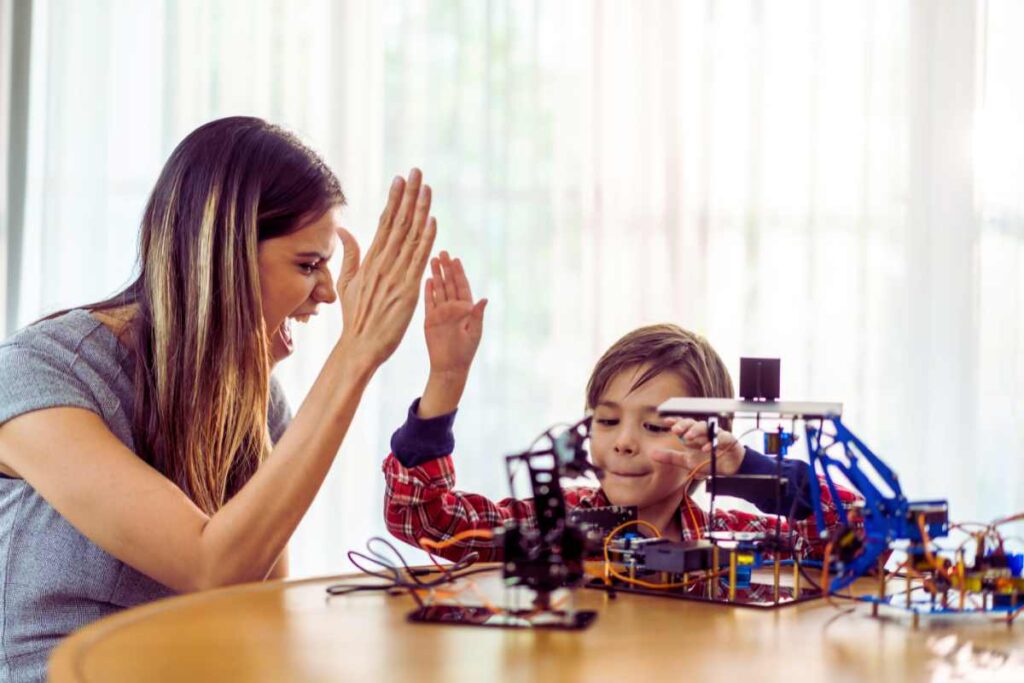 A mother and son share a joyful high five while working on a creative project, representing confidence, encouragement, and emotional growth through connection.