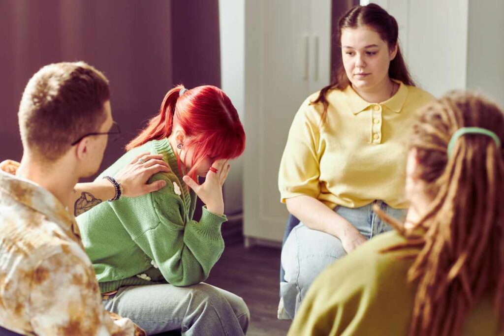 A woman is comforted by a supportive group member as others listen with empathy, representing the power of shared emotional understanding and compassion.