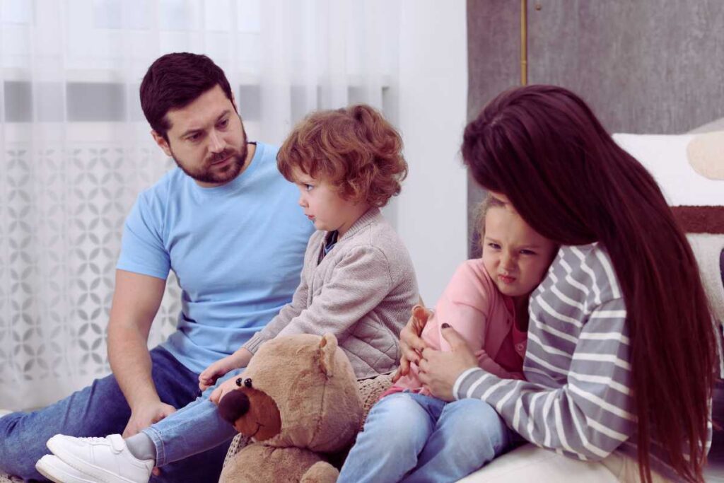 A family sits together on the floor as parents comfort two children, showing empathy and teamwork while helping them manage strong emotions.